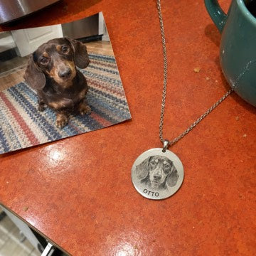 AI concept: A silver OTTO necklace lies on an orange countertop beside the matching dachshund photo.